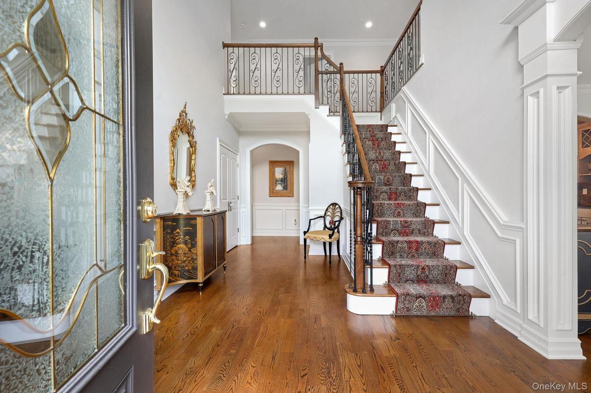 Two-story foyer with hardwood flooring, a grand staircase featuring wood and wrought iron railings, decorative wainscoting, and an arched entryway