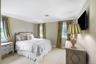 Elegant primary bedroom featuring multiple windows with natural light, neutral wall finishes, and wall-mounted flat-screen television