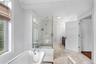 Freestanding clawfoot tub with chrome fixtures, glass-enclosed shower with marble-style tile, light-toned tile flooring, white crown molding, and a da
