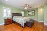 Spacious primary bedroom showcasing soft green walls, hardwood flooring, ceiling fan with integrated lighting, and a framed mirror