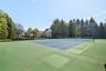Full-sized tennis court with a perimeter fence, surrounded by mature trees