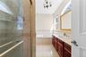 Tiled shower enclosure with a glass door, built-in bathtub, dual windows, and a vanity with an integrated sink and wood-finish cabinetry
