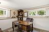 Sophisticated home office featuring a wood-finish desk with carved legs, built-in shelving with display space, large multi-pane windows with natural l