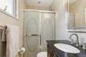 Shower with decorative frosted glass doors, dark countertop vanity with an oval sink, brushed nickel faucet, and a wall-mounted mirror with an ornate 