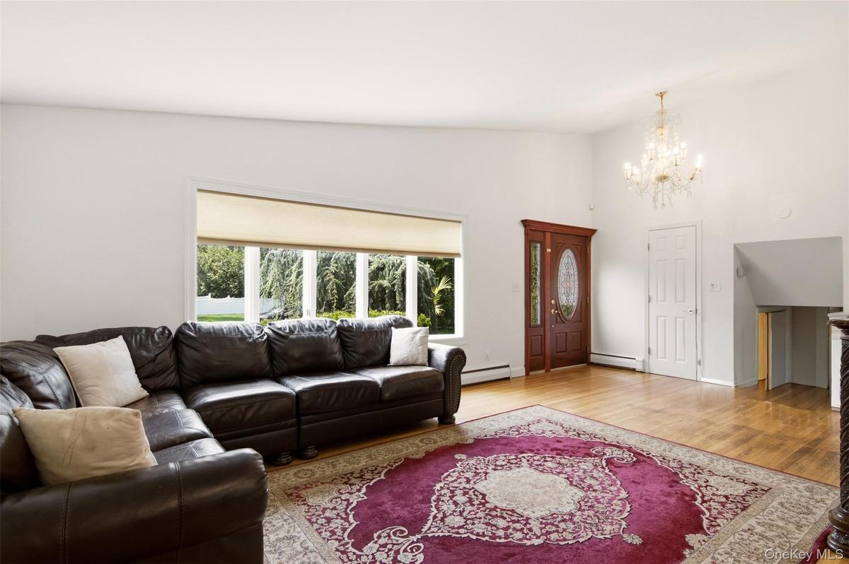 Hardwood flooring, crystal chandelier, decorative front door with oval glass insert, large windows, and white interior walls