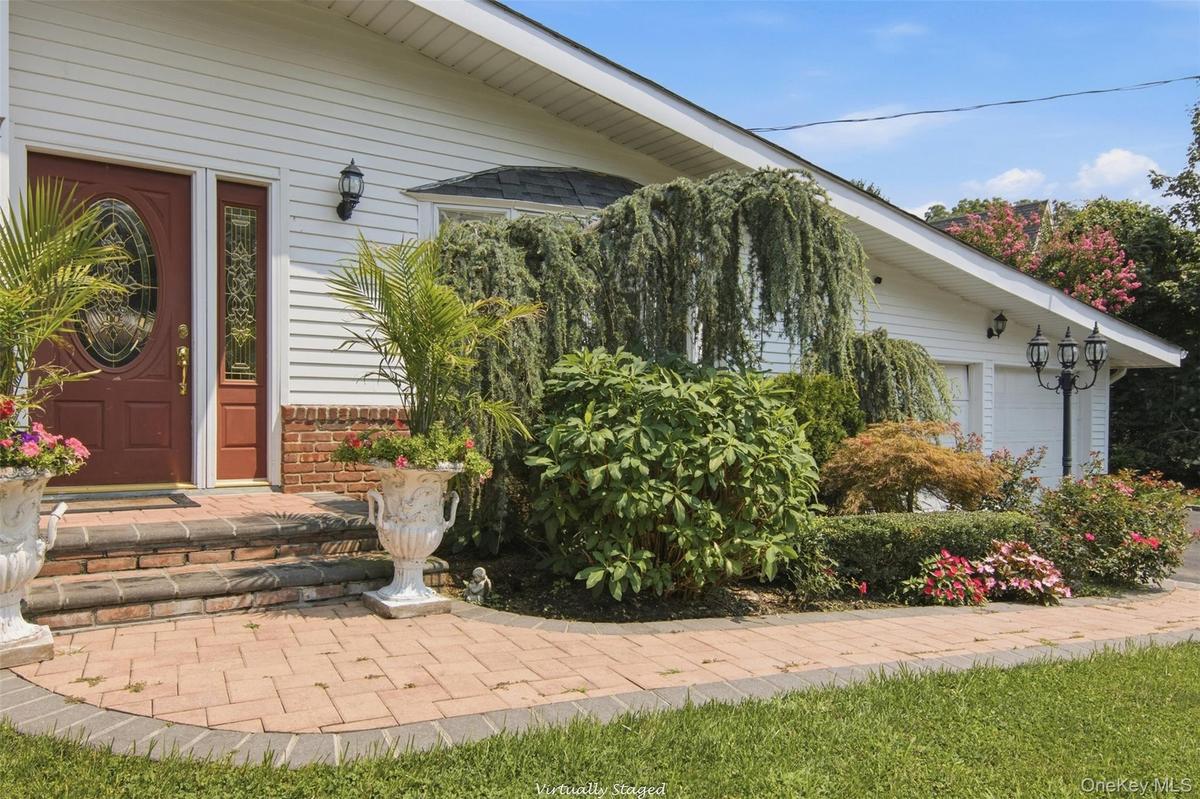 Brick paver walkway with a brick step entry, white siding exterior, and an attached two-car garage
