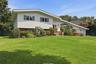 White siding exterior with a brick lower level, featuring a two-car garage, mature landscaping, and an expansive lawn