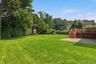 Expansive manicured lawn with mature trees, elevated wood deck with stairs, and a paver patio