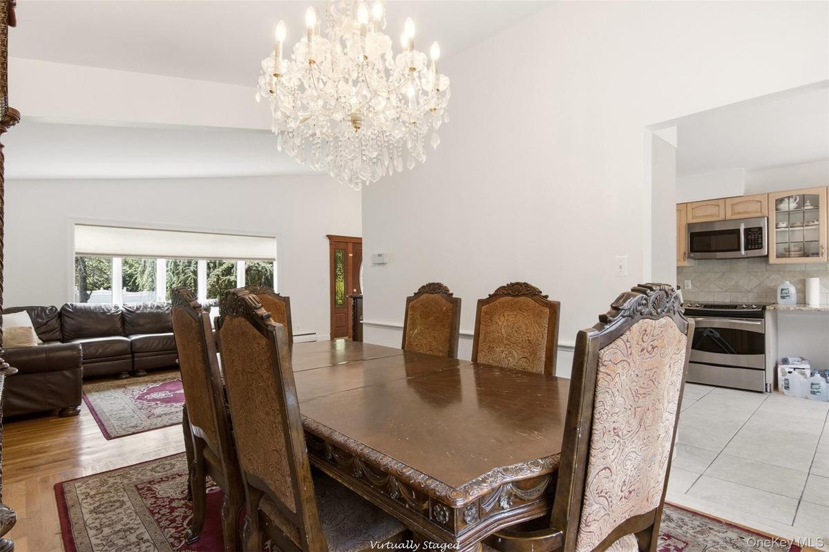 Vaulted ceiling with a crystal chandelier, wood-finish flooring, bay window, kitchen with stainless steel appliances, and wood cabinetry