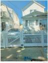 White picket fence with gate, concrete pathway, and residential exterior featuring updated horizontal siding