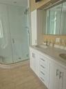 Master Bathroom with double vanity with integrated sinks, white cabinetry and light-toned countertop, mirrored medicine cabinet and stand-alone glass 