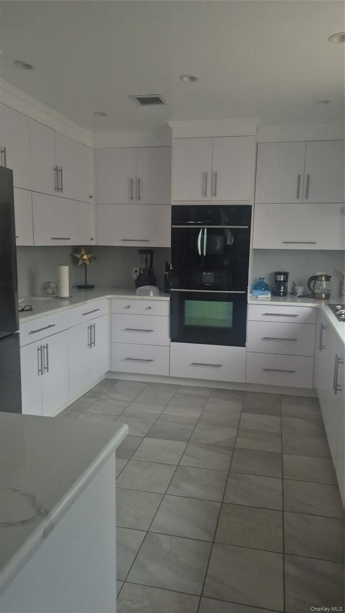 White cabinetry, stone-finish countertops, tile flooring, built-in wall oven, and built-in microwave and dishwasher