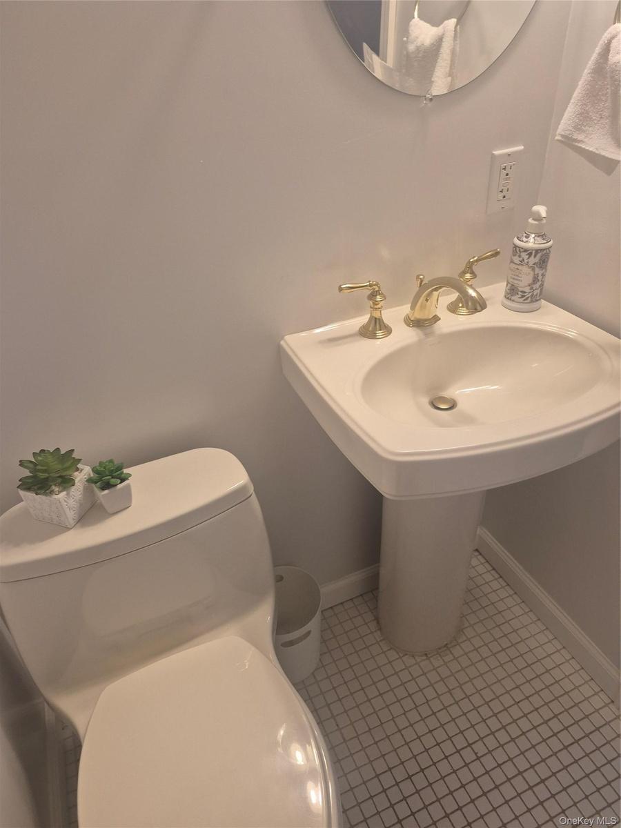 Powder Room with Pedestal sink with brass-finish faucet, white square tile flooring, and a round wall mirror
