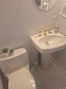 Powder Room with Pedestal sink with brass-finish faucet, white square tile flooring, and a round wall mirror