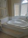 Master Bathroom with corner jetted bathtub with a light-toned surround, white tile wainscoting, an arched window and heated towel rack.