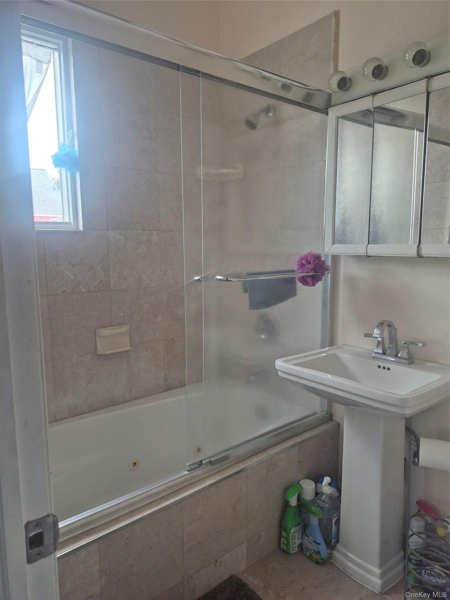 Modern bathroom featuring a frameless glass shower enclosure with chrome hardware, pedestal sink with single-handle faucet, tiled surround, and a wind