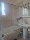 Modern bathroom featuring a frameless glass shower enclosure with chrome hardware, pedestal sink with single-handle faucet, tiled surround, and a wind