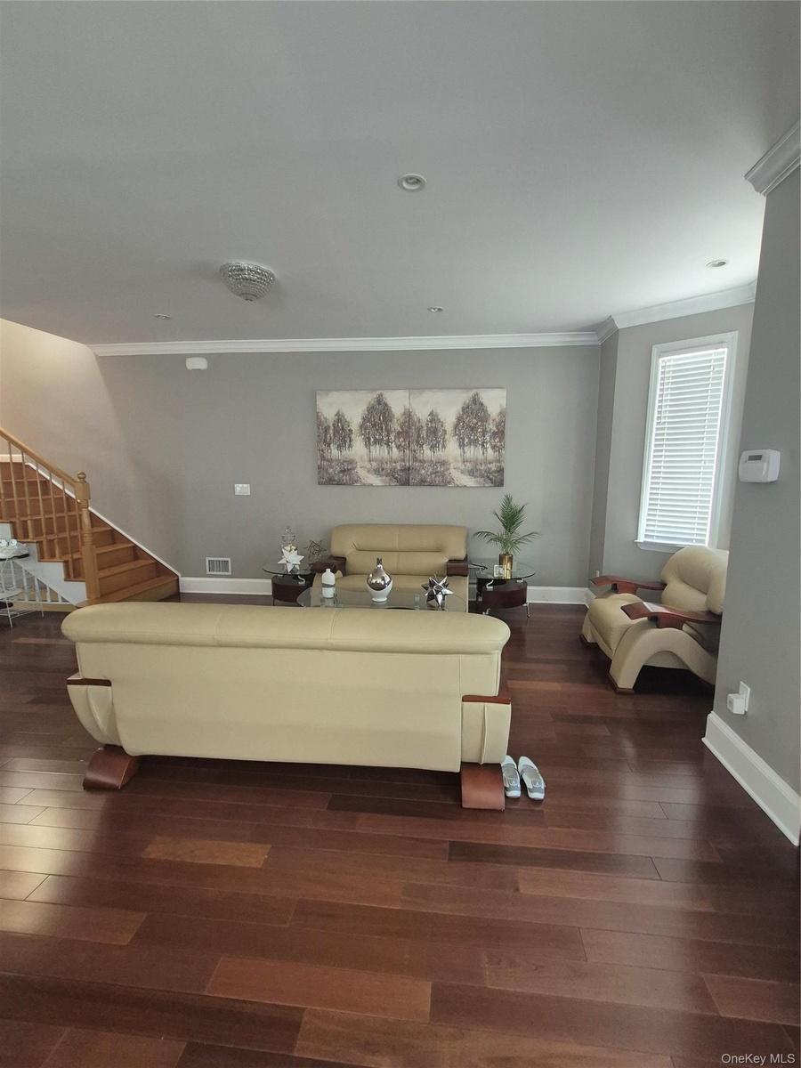 Spacious living room area with hardwood flooring, recessed lighting, crown molding, and a large window with blinds