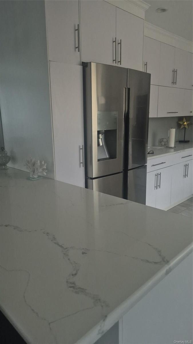 White cabinetry with brushed nickel hardware and stone-finished countertops and bar stools with stainless steel refrigerator