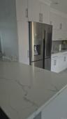 White cabinetry with brushed nickel hardware and stone-finished countertops and bar stools with stainless steel refrigerator
