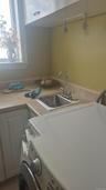 Laundry and utility area featuring a stainless steel sink, chrome faucet, and overhead cabinetry