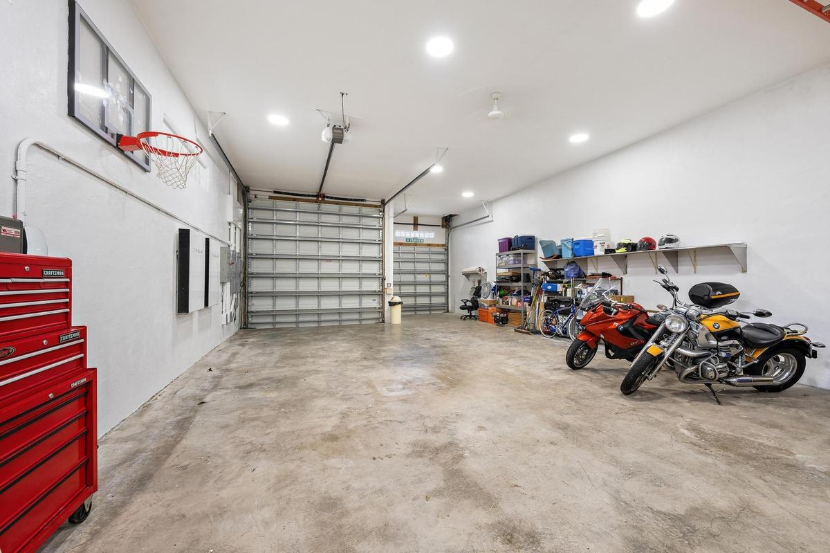 Spacious garage featuring polished concrete flooring, overhead lighting, wall-mounted storage cabinetry, a basketball hoop, and ample room for multipl
