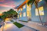 Multi-story exterior with large windows, concrete hardscaping, artificial turf accents, and mature palm trees