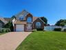 Brick and siding exterior with arched windows, a paver driveway, and a manicured lawn