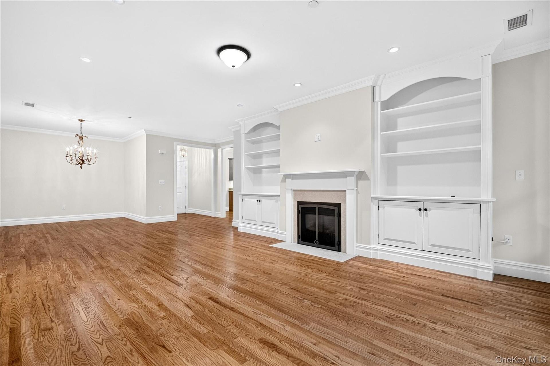 Hardwood flooring, fireplace with mantel, built-in shelving, crown molding, and chandelier