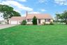 Expansive front lawn, two-car garage, paved driveway, mature trees, and a brick chimney