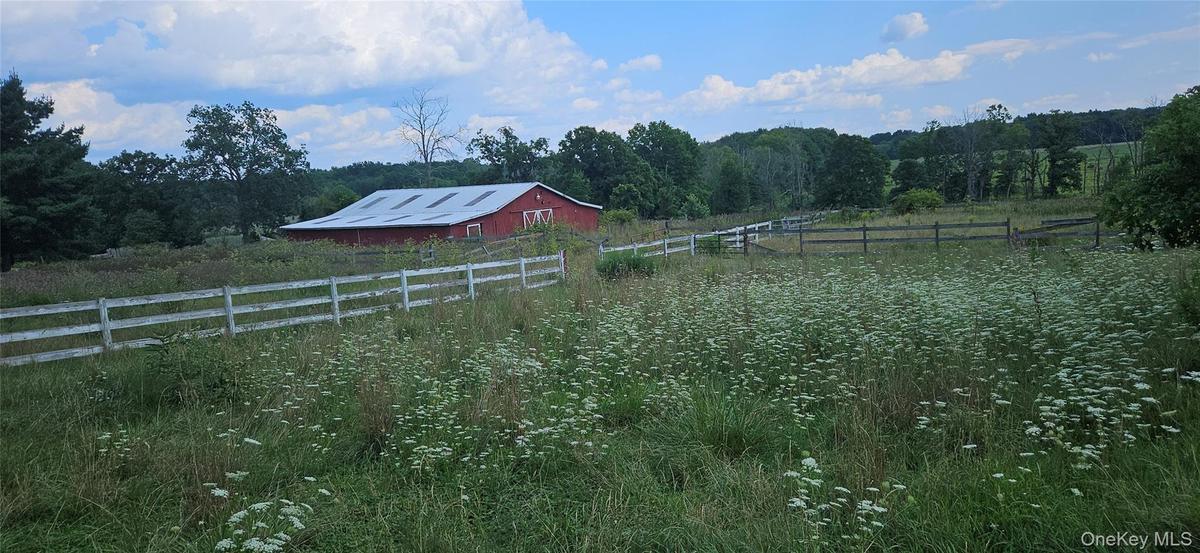 Expansive green fields, red barn with a metal roof, and white perimeter fencing