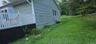 Exterior siding with window, white deck railing, and sloped grassy area