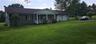Ranch-style residence featuring a covered front porch with white railings, a two-car garage, and a charcoal shingle roof