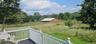 Deck with white railing and dark composite flooring, overlooking expansive fields, a red barn, and mature trees