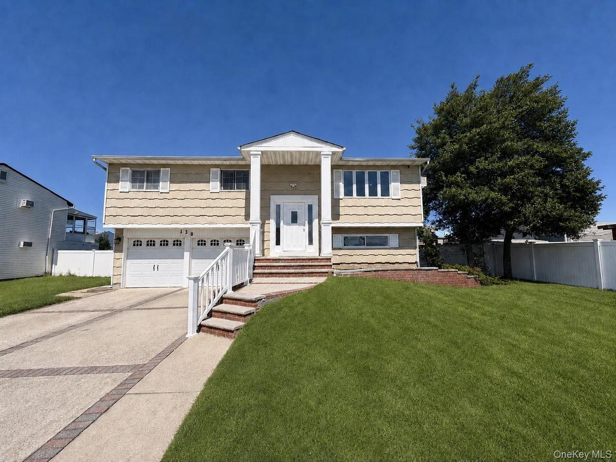 Split-level residence featuring a two-car garage, concrete driveway with brick accents, and a covered front entry with white columns