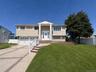 Split-level residence featuring a two-car garage, concrete driveway with brick accents, and a covered front entry with white columns