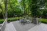 Expansive outdoor deck with light gray decking and white railing, surrounded by mature trees and manicured lawn