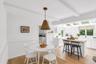 White shaker cabinetry, light wood-finish flooring, exposed ceiling beams, a central island with wood butcher block countertop, and multiple skylights