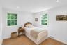 Recessed lighting illuminates a room with two large windows and a woven area rug
