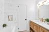 Bathroom featuring a natural wood-finish vanity with a white countertop, gold-toned faucet and cabinet hardware, and a framed mirror with a modern lig