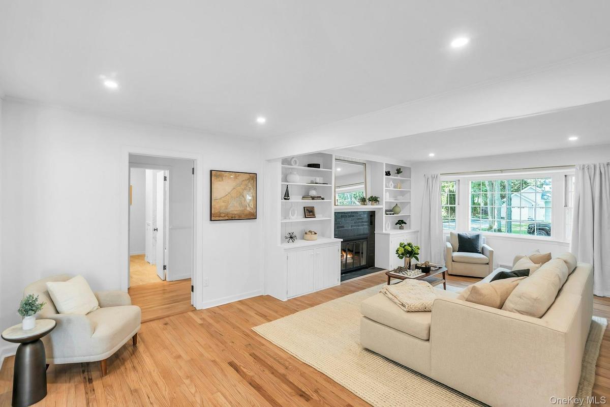 Recessed lighting illuminates the living area, featuring wood-finish flooring and a fireplace with built-in shelving