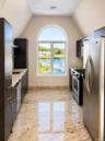 Arched window with water scenery, dark wood-finish cabinetry, stainless steel appliances, light-toned countertop, and polished tile flooring