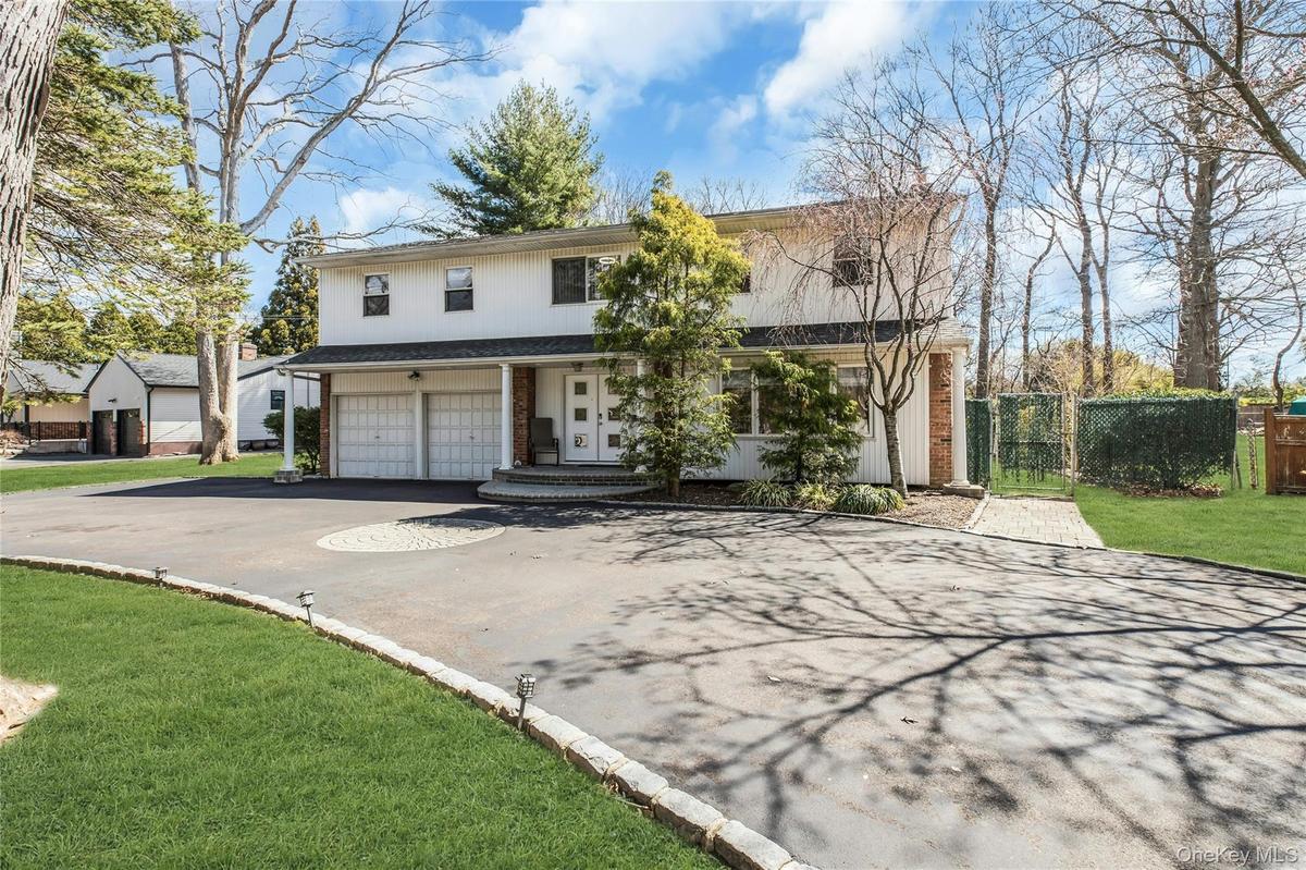 Two-story residence with a two-car garage, circular driveway with paver accents, front porch, and mature trees