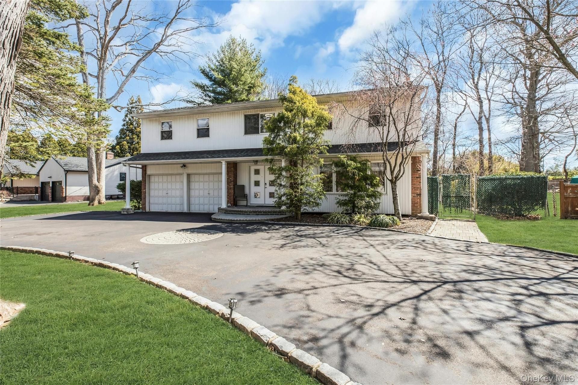 Two-story residence with a two-car garage, circular driveway with paver accents, front porch, and mature trees
