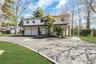 Two-story residence with a two-car garage, circular driveway with paver accents, front porch, and mature trees