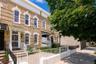 Brick facade with contrasting stone banding, arched windows, and a white wrought iron fence