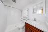 White textured shower tile, integrated shower system, white countertop with integrated sink, wood-finish vanity, and wall-mounted storage cabinet