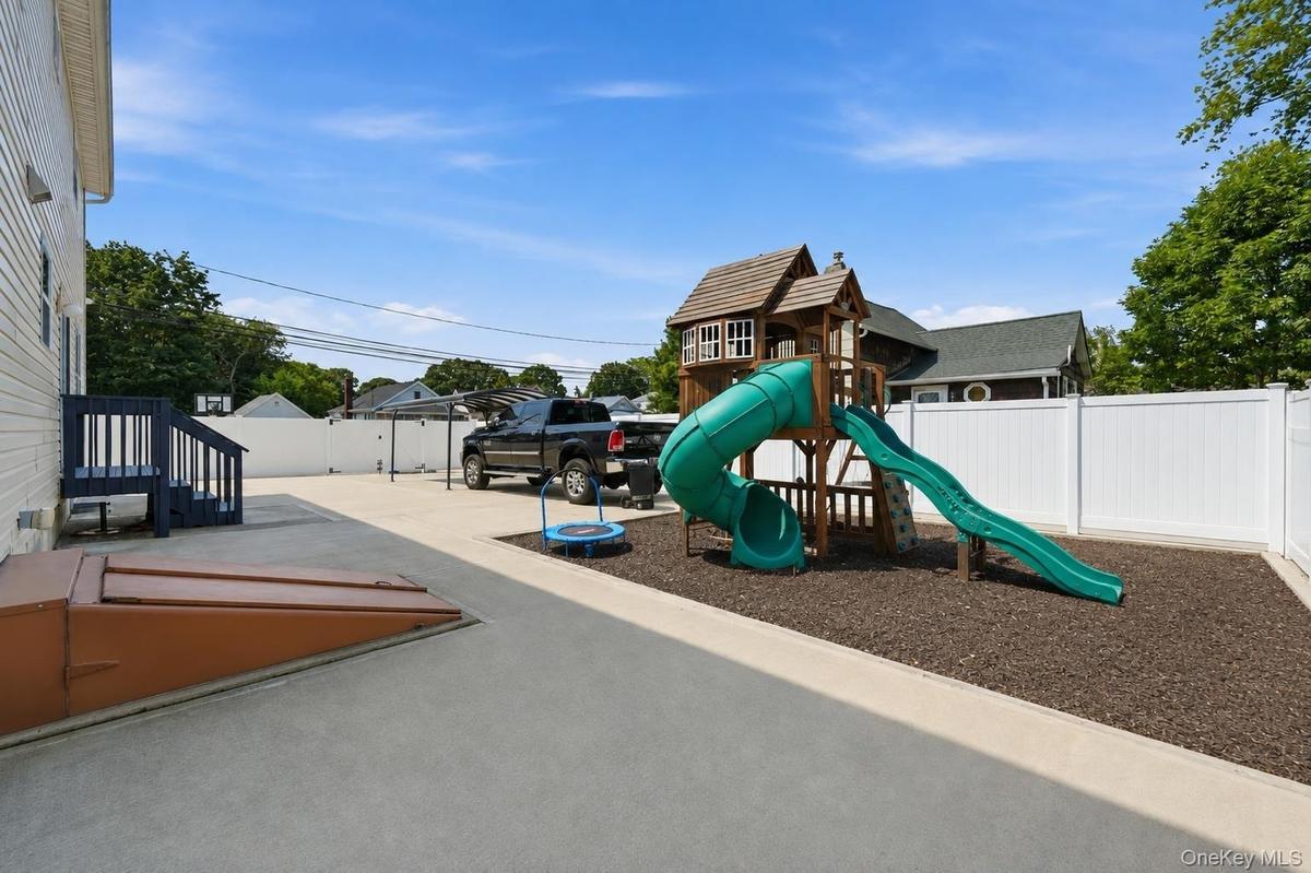 Spacious concrete patio with a separate mulched play area, a privacy fence, and an exterior basement entry