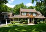 Expansive lawn with mature landscaping, a two-car garage with arched doors, a covered entry with white columns, and wood shake siding with white trim