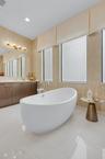 Freestanding white soaking tub with polished chrome fixtures, set on large format tile flooring